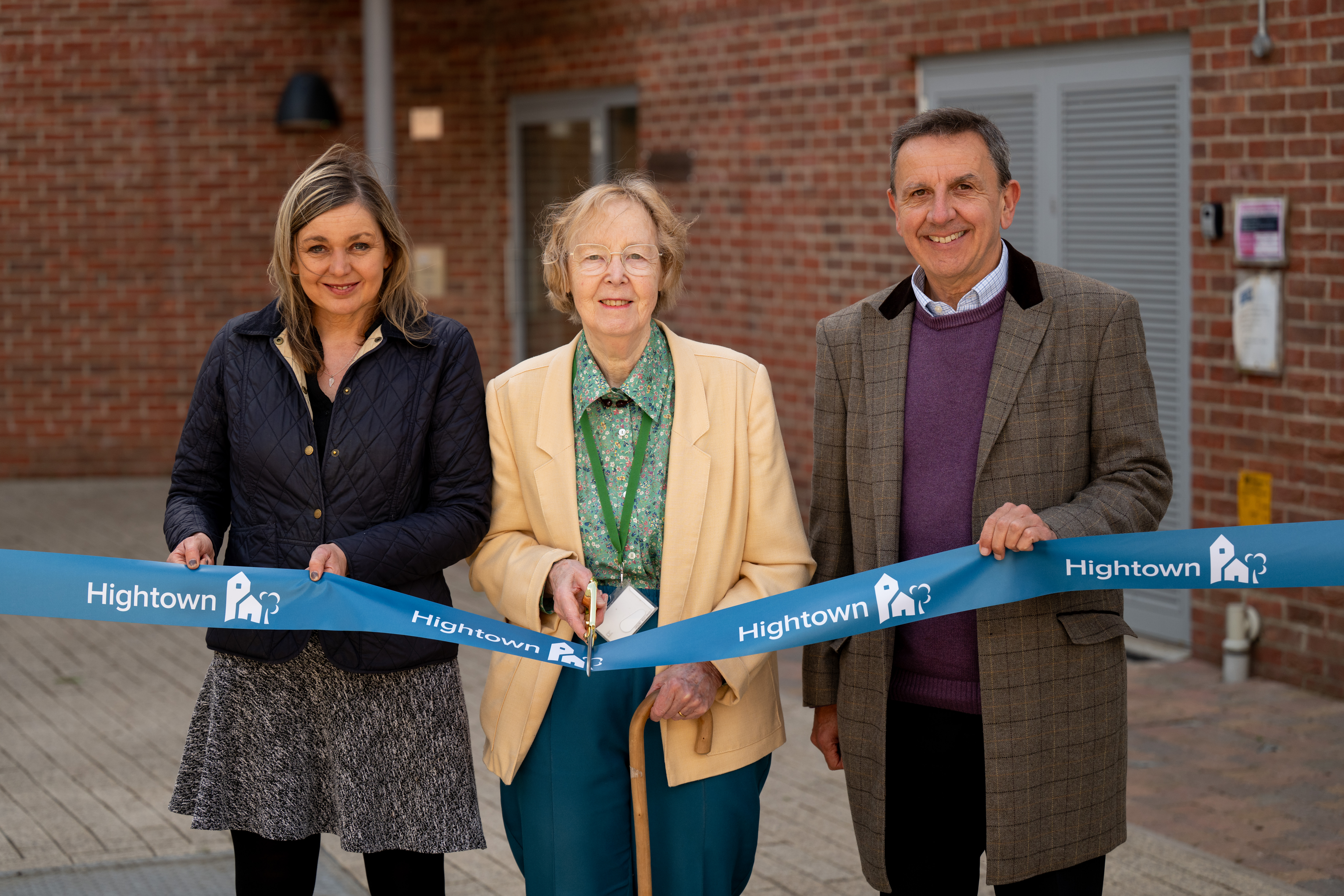 Two women and a man standing to cut a ribbon in front of the new flats