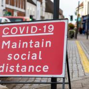Red road sign with COVID-19 maintain social distance text in white