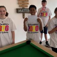 Four young people standing by a pool table holding smoothie maker and juicer