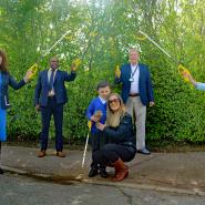 Two women and two man stand in a semi-circle with litter picking equipment held up up above a primary school child and his mother