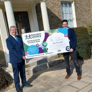 pictured are councillor Jonathan Kaye on the left and Nick Phipps on the right holding a board that displays the total fundraising amount for the east herts lottery so far of £120,893.40