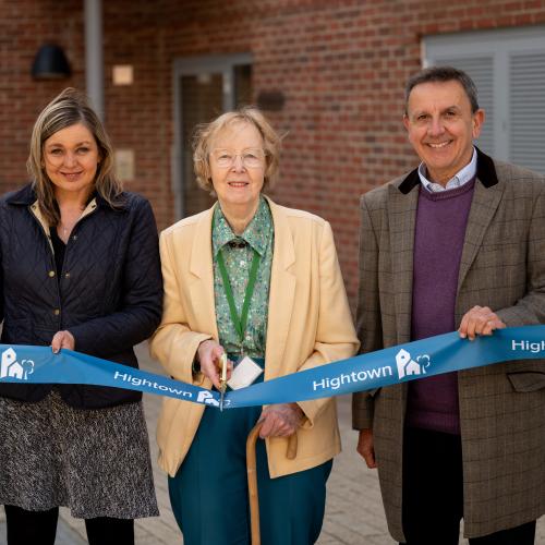 Two women and a man standing to cut a ribbon in front of the new flats